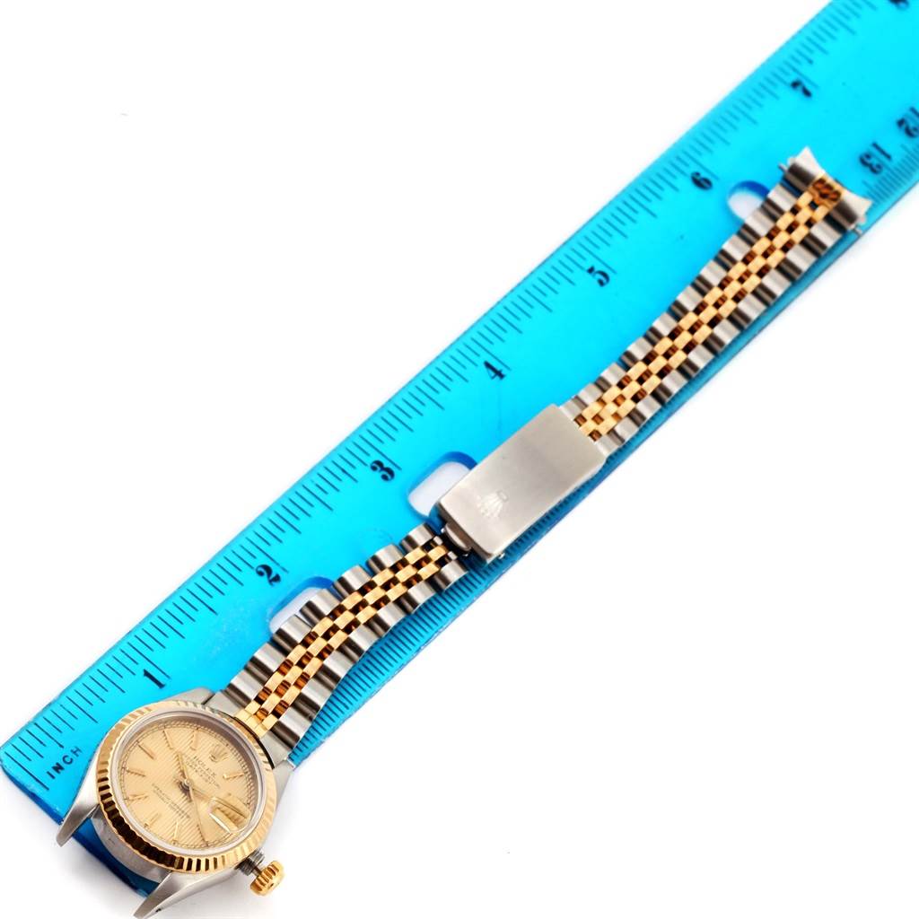 The Rolex Datejust 69173 Women
s Stainless Steel Champagne Dial 69173 Women
s Stainless Steel Champagne Dial watch is shown from above, featuring the face, bezel, bracelet, and clasp laid next to a ruler.