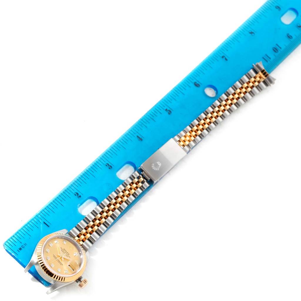 The Rolex Datejust 79163 Women's Steel and Gold (two tone) Champagne Dial 79163 Women's Steel and Gold (two tone) Champagne Dial watch model is shown from a top-down angle, highlighting its face, bracelet, and clasp alongside a blue ruler for scale.