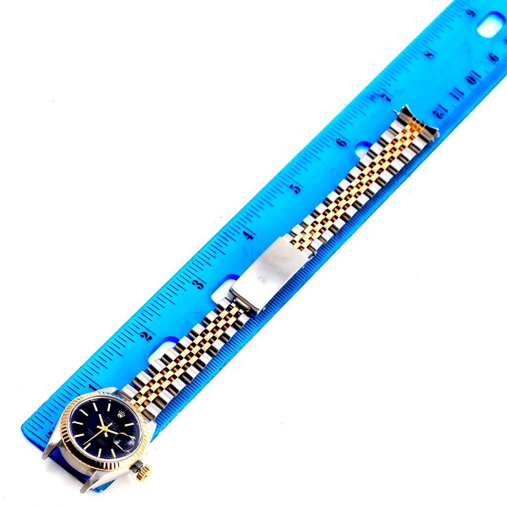 This image shows a Rolex Datejust 69173 Women's Stainless Steel Black Dial 69173 Women's Stainless Steel Black Dial watch laying alongside a blue ruler, highlighting its face, case, and bracelet.