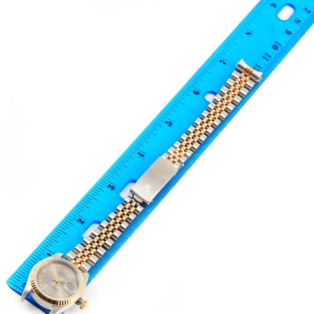 The Rolex Datejust 69173 Women
s Stainless Steel Grey Dial 69173 Women
s Stainless Steel Grey Dial watch is shown from an overhead angle, displaying its face, bezel, bracelet, and clasp alongside a blue ruler.