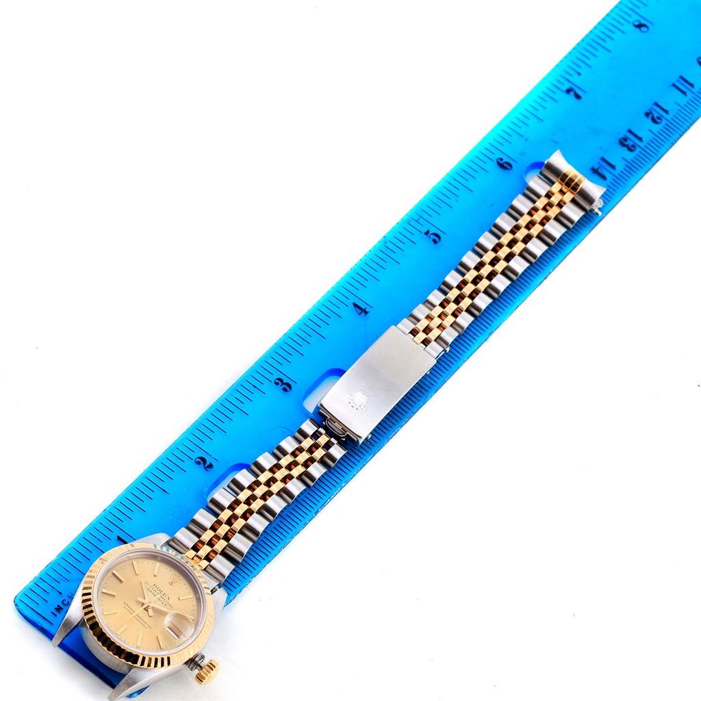 A Rolex Datejust 69173 Women
s Stainless Steel Champagne Dial 69173 Women
s Stainless Steel Champagne Dial watch is shown laid flat alongside a blue ruler, displaying the face, band, and clasp.