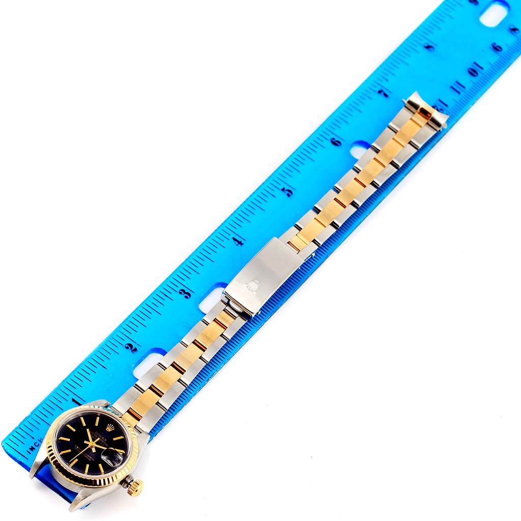 The image shows a Rolex Datejust 69173 Women
s Stainless Steel Black Dial 69173 Women
s Stainless Steel Black Dial watch laid flat next to a ruler, displaying its face, strap, and clasp.