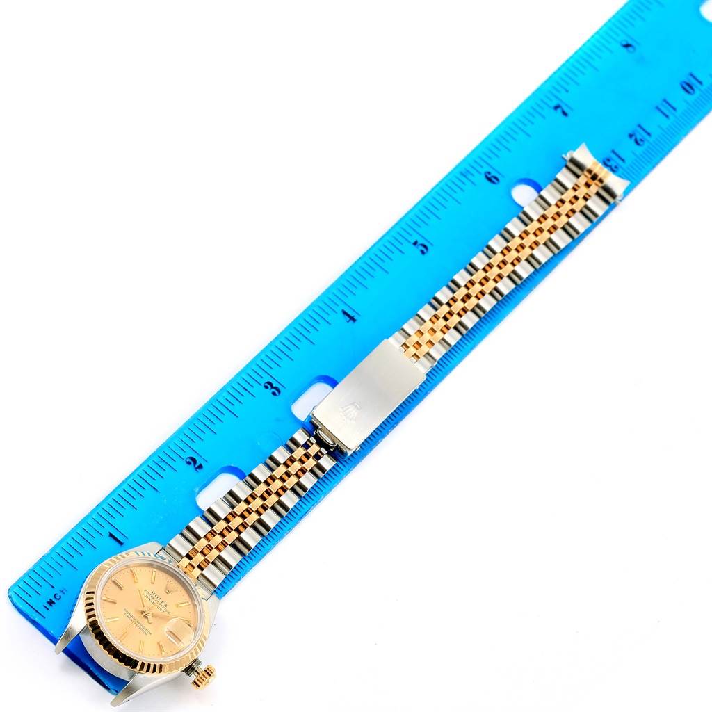 This image shows a Rolex Datejust 69173 Women
s Stainless Steel Champagne Dial 69173 Women
s Stainless Steel Champagne Dial watch and its gold and silver bracelet, placed beside a blue ruler for measurement.