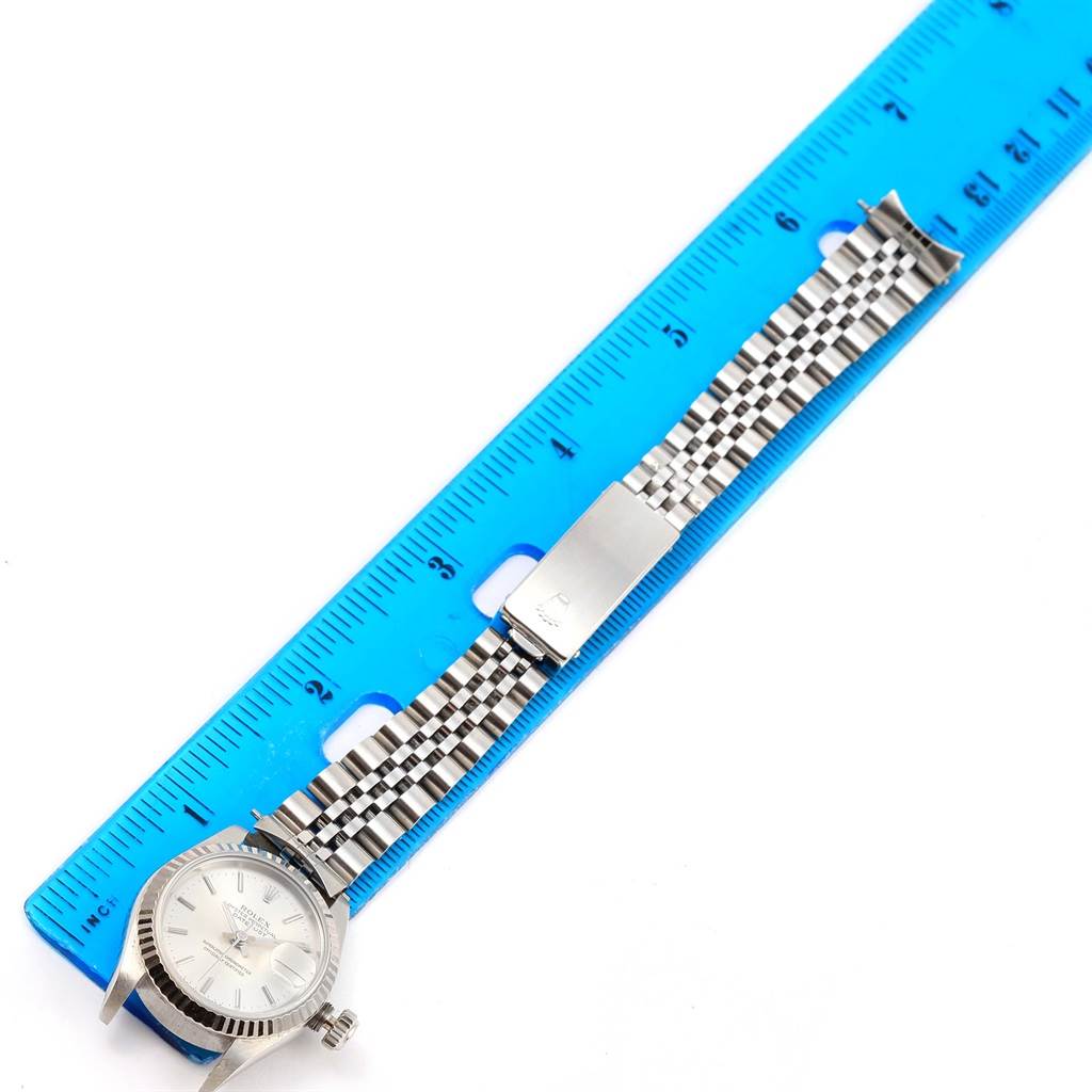 The Rolex Datejust 69174 Women's Stainless Steel Silver Dial 69174 Women's Stainless Steel Silver Dial watch is laid flat next to a blue ruler, showing its face, crown, and band with a clasp.