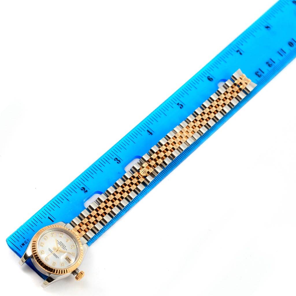 The image shows a Rolex Datejust 179173 Women's Steel and Gold (two tone) Mother of Pearl Dial 179173 Women's Steel and Gold (two tone) Mother of Pearl Dial watch placed flat next to a blue ruler, revealing the face, crown, and full bracelet.