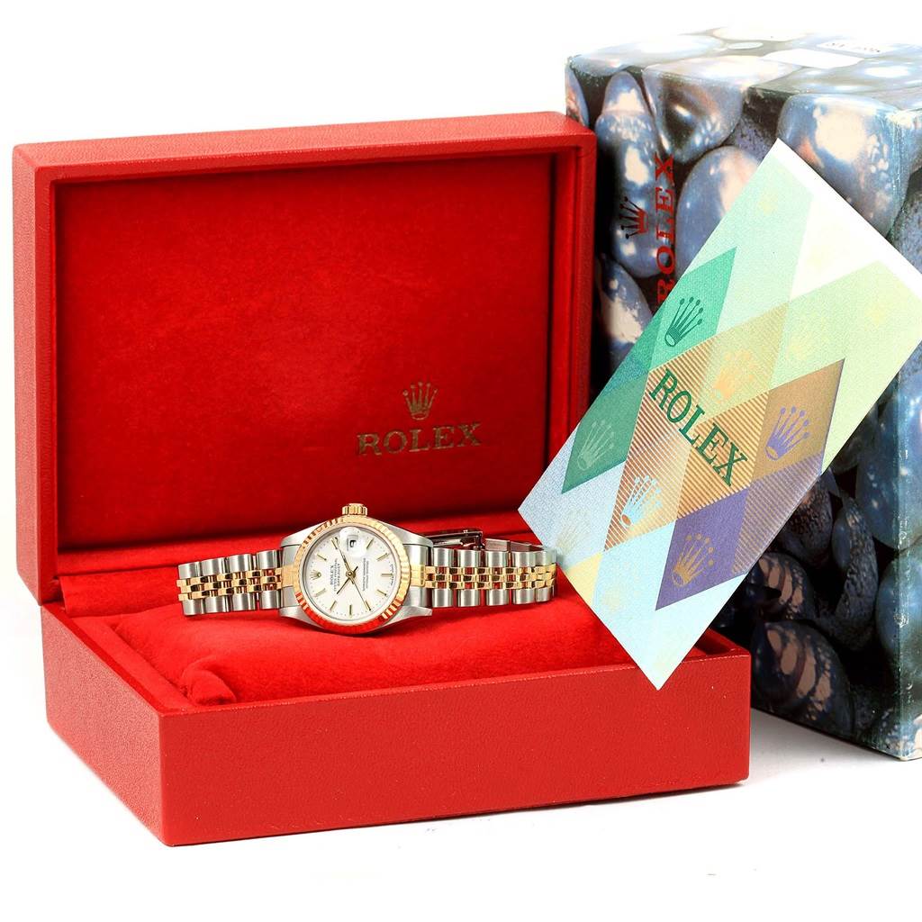 The Rolex Datejust 79173 Women's Steel and Gold (two tone) White Dial 79173 Women's Steel and Gold (two tone) White Dial watch is displayed in an open red box, accompanied by a multi-colored booklet and the outer packaging box is to the side.