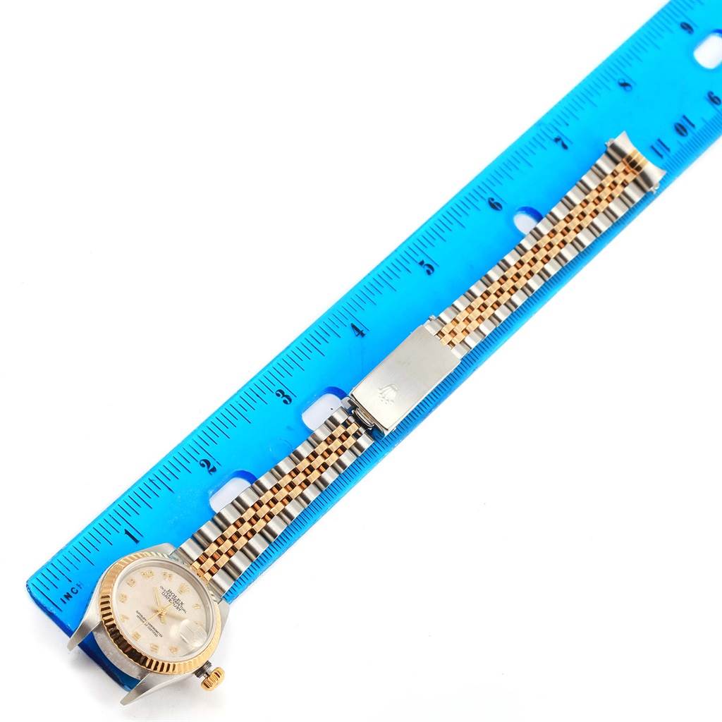 The Rolex Datejust 79173 Women's Steel and Gold (two tone) Beige Dial 79173 Women's Steel and Gold (two tone) Beige Dial watch is shown face-up with its bracelet extended alongside a blue ruler for size reference.