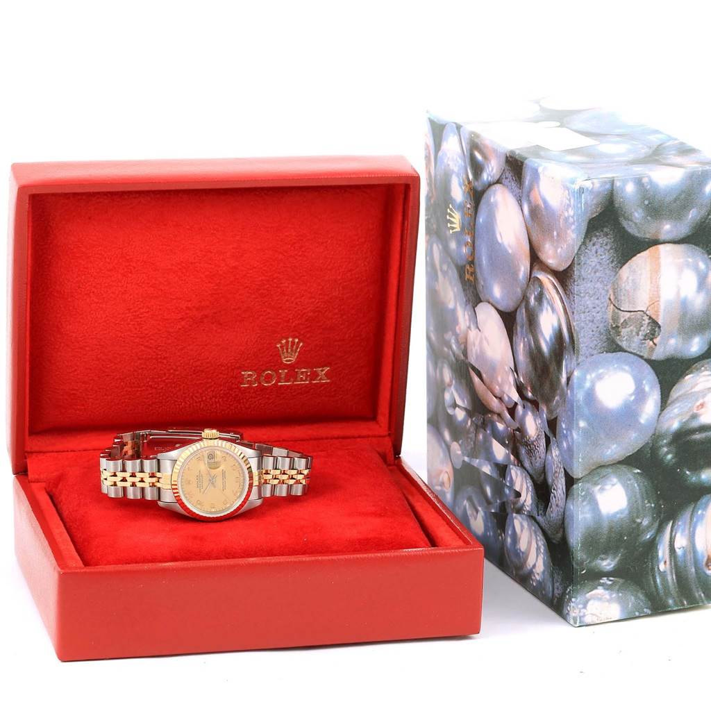 A Rolex Datejust 69173 Women's Stainless Steel Champagne Dial 69173 Women's Stainless Steel Champagne Dial watch is shown from the front inside a red box with a patterned outer box beside it.