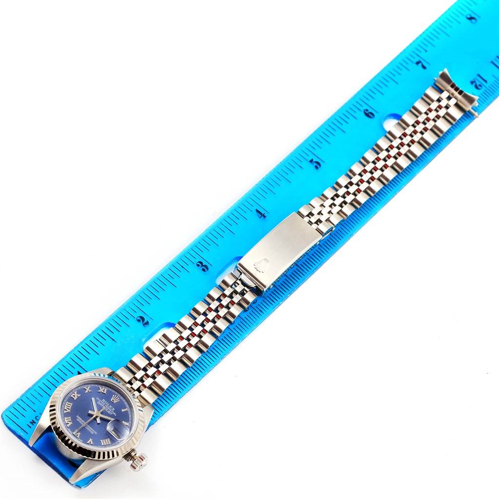 This is a top-down view of a Datejust model Rolex watch showing its dial, bracelet, and clasp next to a blue ruler.