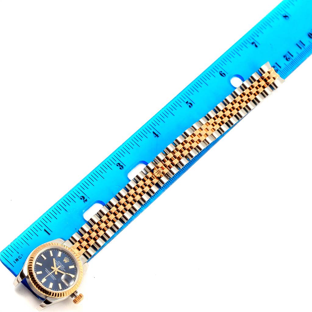 This image displays a Rolex Datejust 179173 Women's Steel and Gold (two tone) Blue Dial 179173 Women's Steel and Gold (two tone) Blue Dial watch with its bracelet against a blue ruler, measuring approximately 7.5 inches.