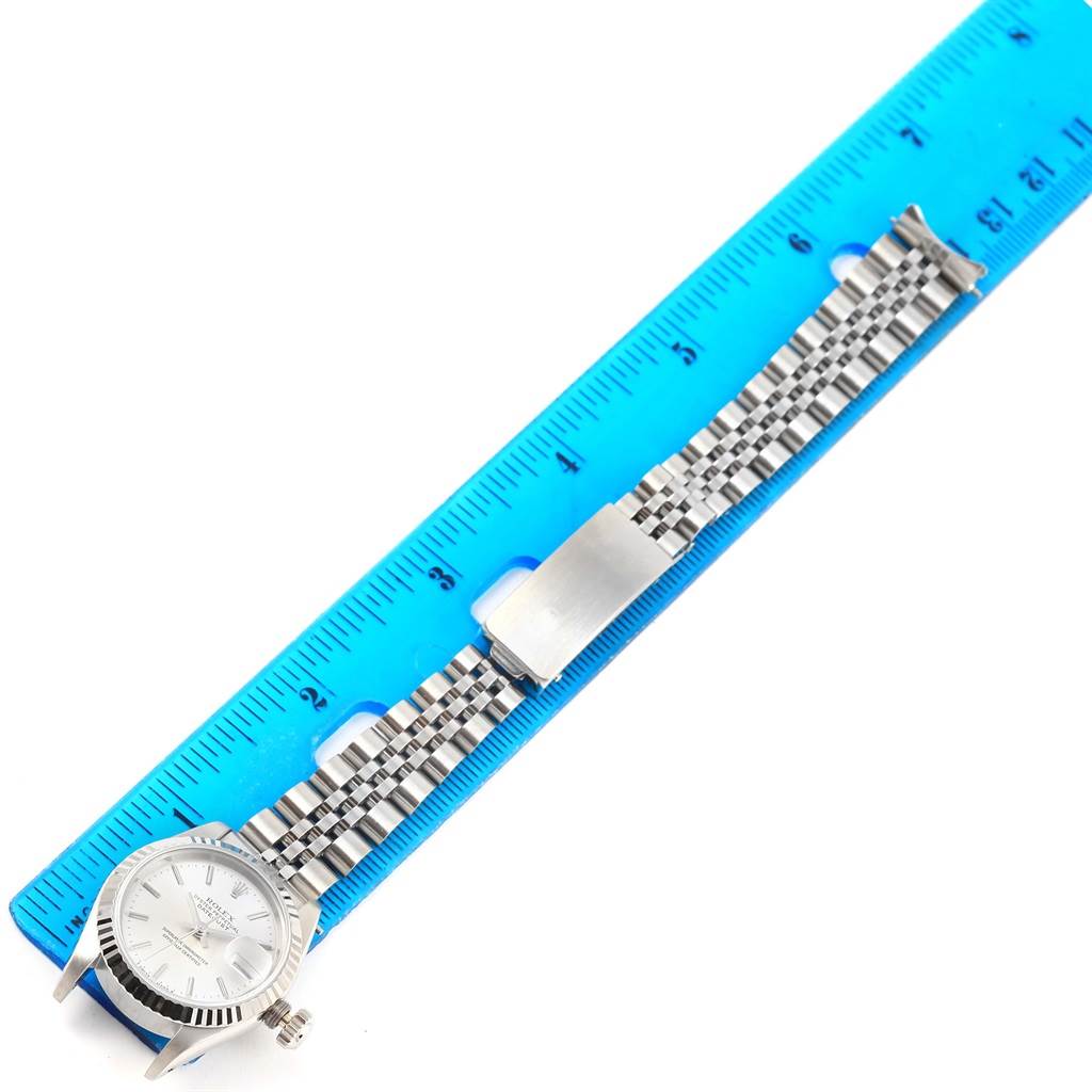 The image shows the side view of a Rolex Datejust 69174 Women's Stainless Steel Silver Dial 69174 Women's Stainless Steel Silver Dial watch with its case, dial, crown, and bracelet next to a ruler.