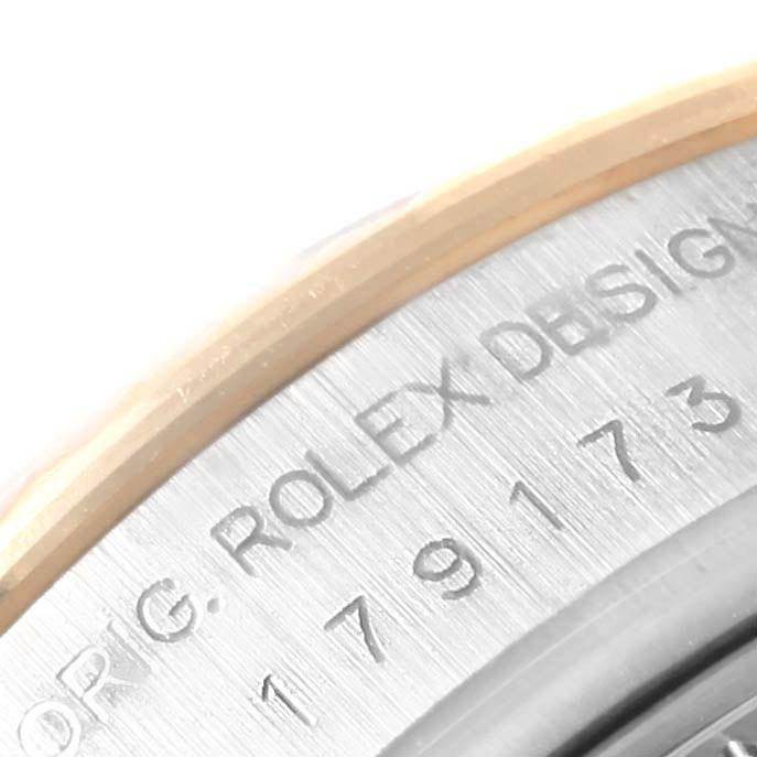 The image shows a close-up of the case side of a Rolex Datejust 179173 Women
s Steel and Gold (two tone) Black Dial 179173 Women
s Steel and Gold (two tone) Black Dial, featuring part of the engraved serial number and "ROLEX DESIGN."