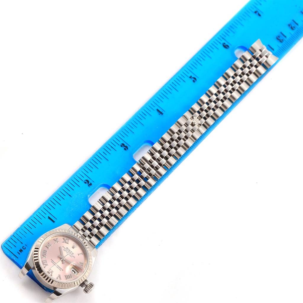 A Rolex Datejust 179174 Women's Stainless Steel Pink Dial 179174 Women's Stainless Steel Pink Dial watch is pictured from above, showing the face, bezel, and metal bracelet, with a ruler to measure the band length.