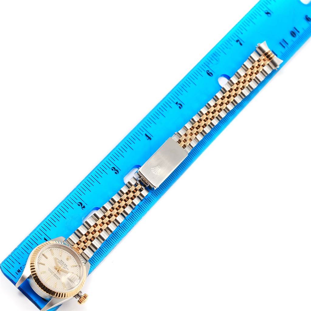 The Rolex Datejust 79173 Women's Steel and Gold (two tone) Silver Dial 79173 Women's Steel and Gold (two tone) Silver Dial watch is shown from a top-down angle with its entire band, clasp, and face visible against a ruler.