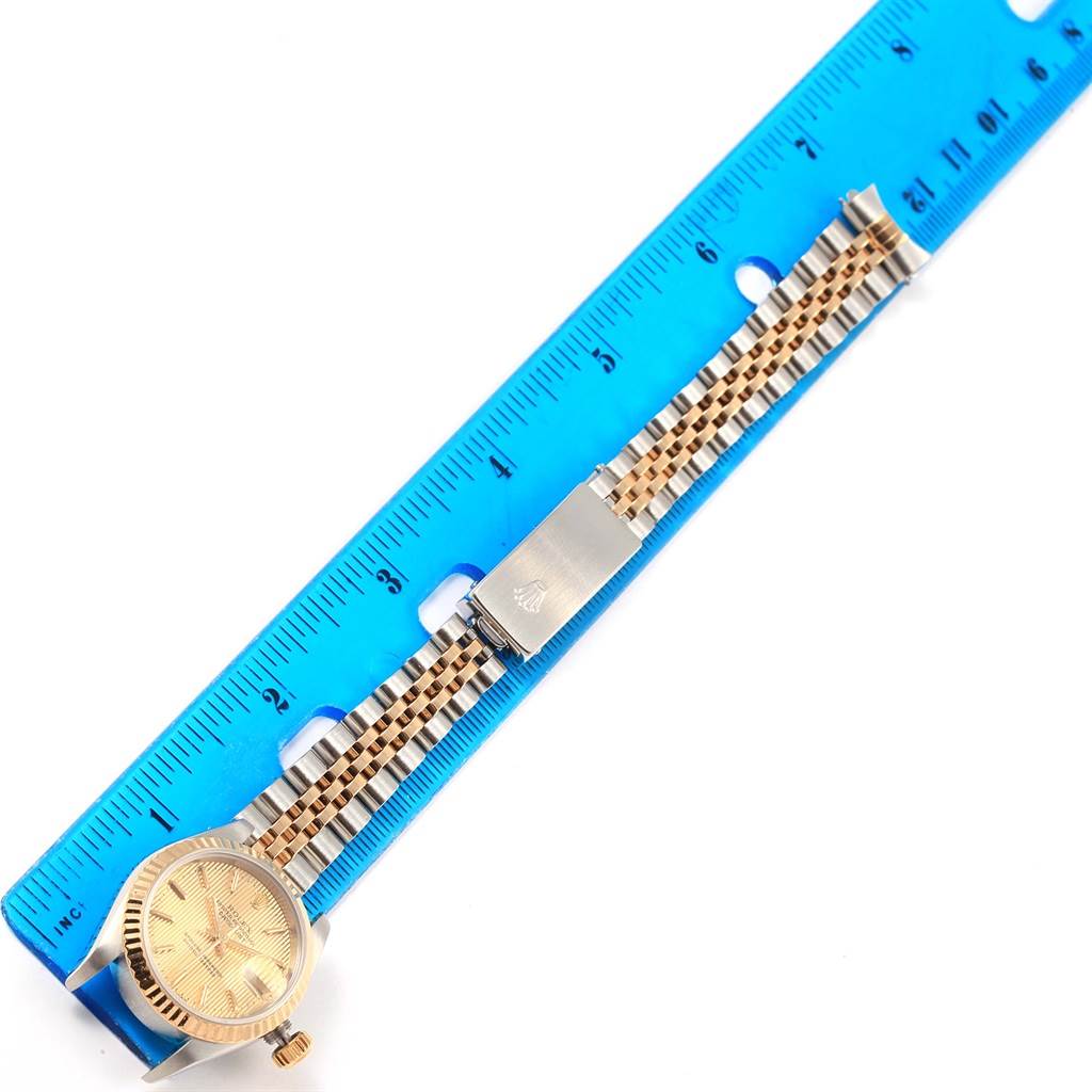 The image shows a Rolex Datejust 79173 Women's Steel and Gold (two tone) Champagne Dial 79173 Women's Steel and Gold (two tone) Champagne Dial watch laid flat next to a ruler, highlighting its band and bezel from a top-down angle.