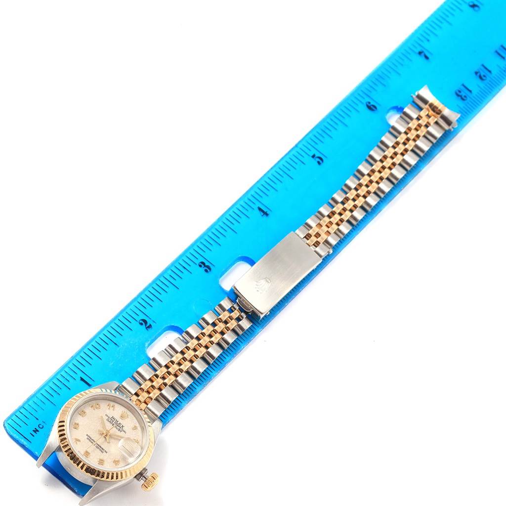The image shows a Rolex Datejust 79173 Women's Steel and Gold (two tone) Beige Dial 79173 Women's Steel and Gold (two tone) Beige Dial watch laid flat with the face, bracelet, and clasp visible, aligned next to a blue ruler for measurement.