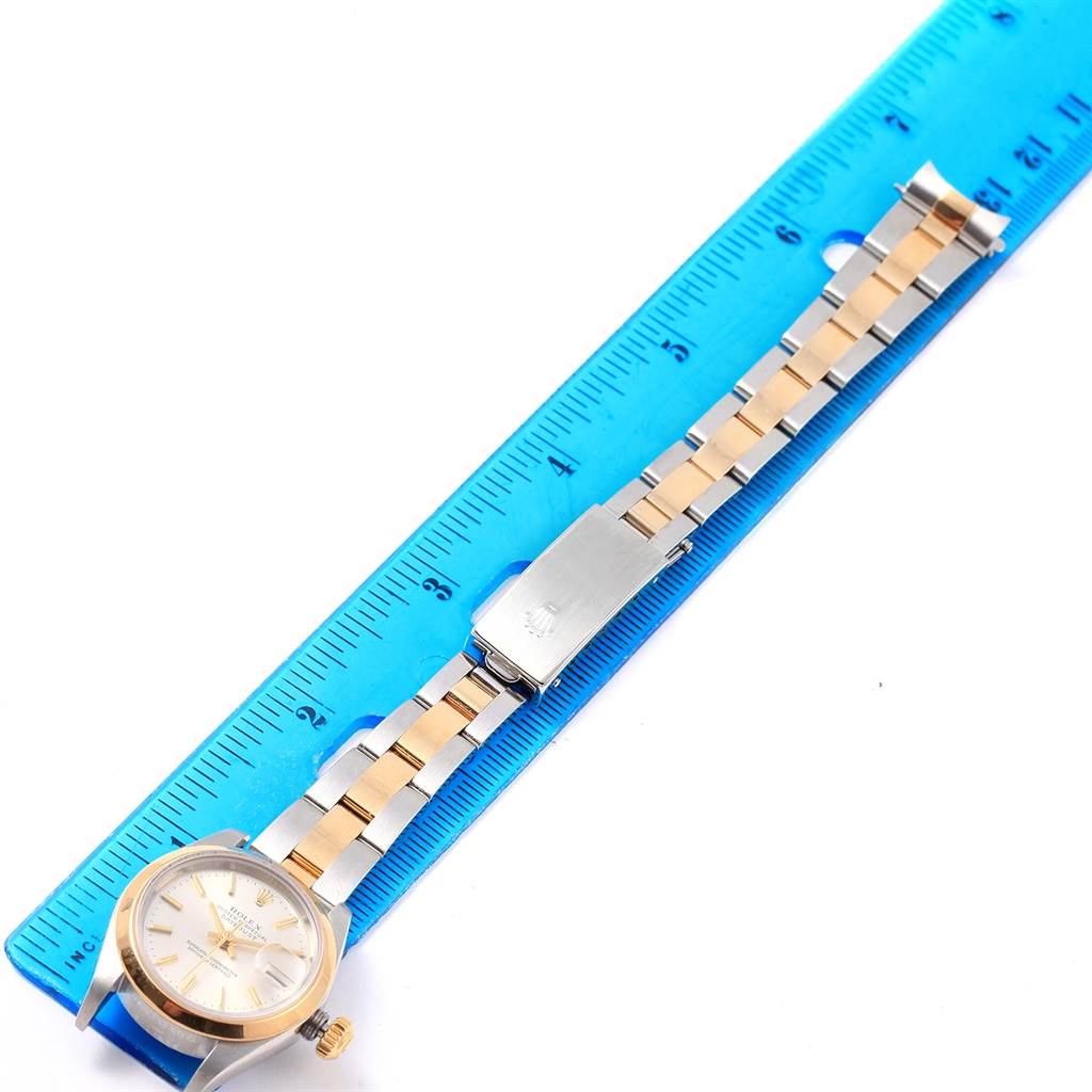 The Rolex Datejust 79163 Women's Steel and Gold (two tone) Silver Dial 79163 Women's Steel and Gold (two tone) Silver Dial watch is laid flat with its face, bracelet, and clasp visible next to a blue ruler for scale.