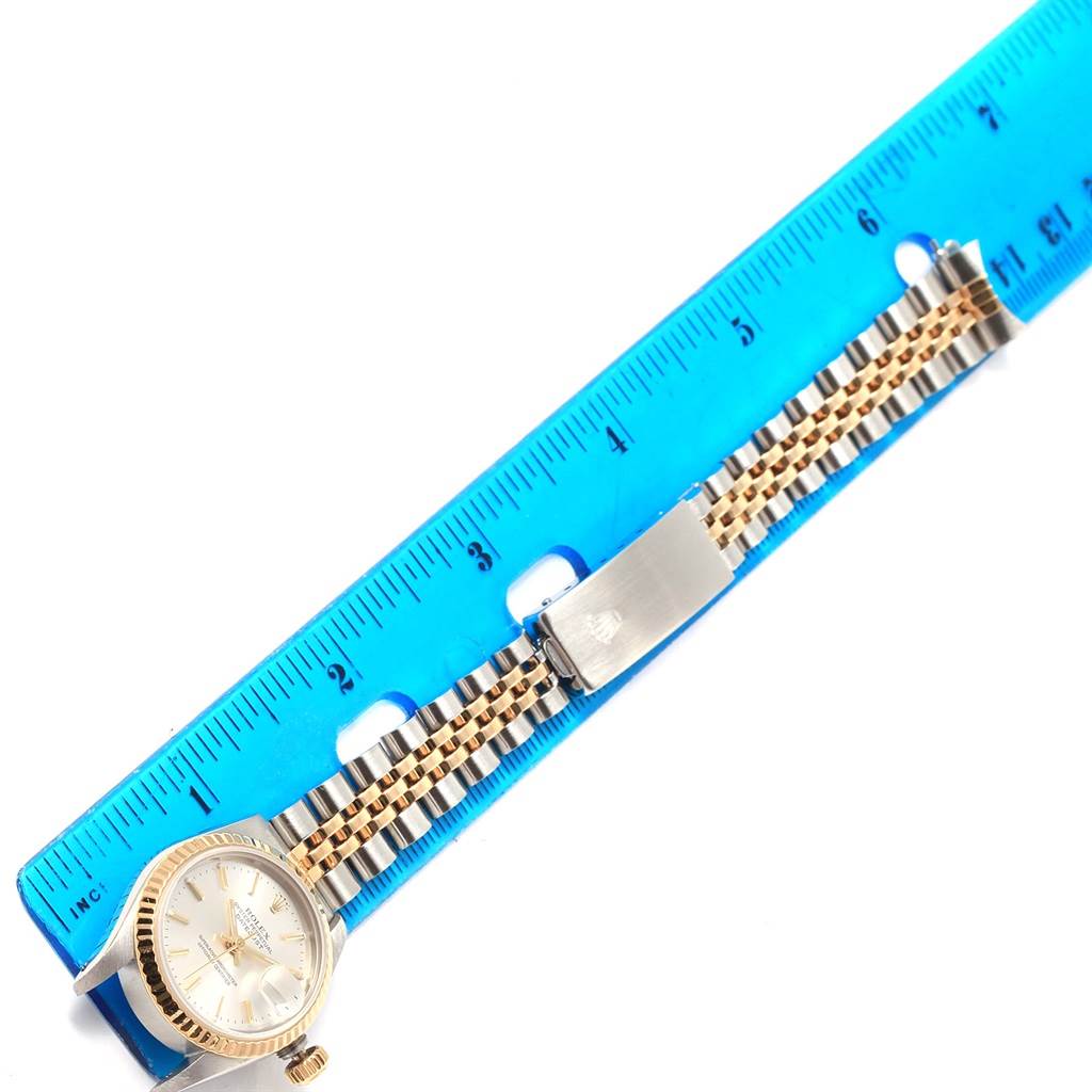 The Rolex Datejust 69173 Women's Stainless Steel Silver Dial 69173 Women's Stainless Steel Silver Dial watch is shown from an overhead view, highlighting the face, bezel, band, and clasp alongside a ruler for scale.