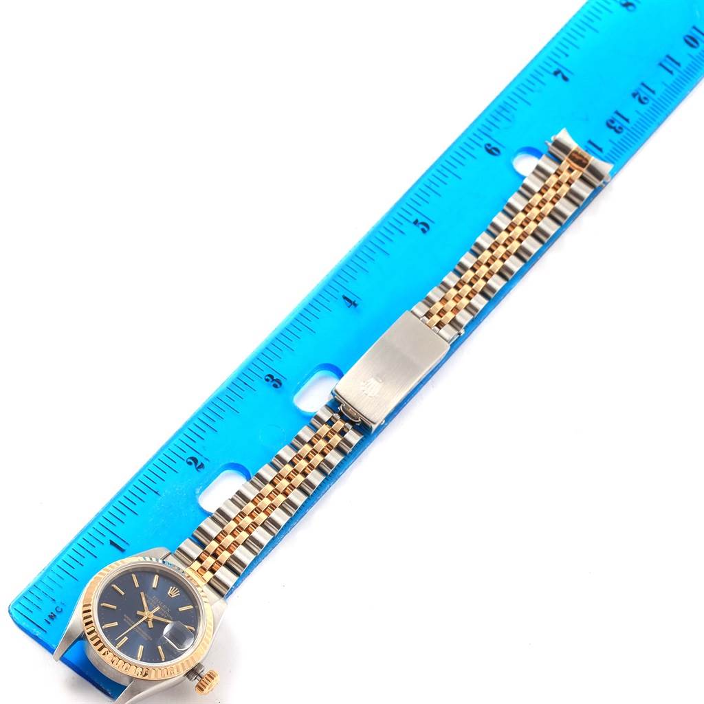 The Rolex Datejust 69173 Women's Stainless Steel Blue Dial 69173 Women's Stainless Steel Blue Dial watch is shown laid flat with a metal and gold bracelet strap next to a blue ruler for measurement.