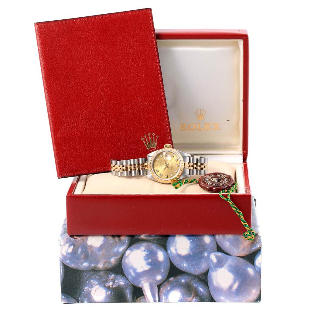 The Rolex Datejust 69173 Women's Stainless Steel Champagne Dial 69173 Women's Stainless Steel Champagne Dial watch and its accessories, including a red case, authentication tag, and booklet, are shown from a front angle.