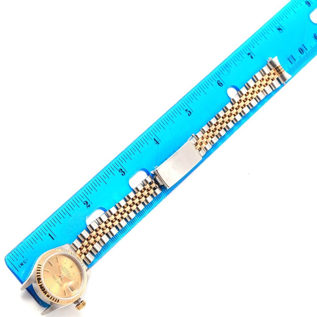 The image shows a top-down view of a Rolex Datejust 79173 Women's Steel and Gold (two tone) Champagne Dial 79173 Women's Steel and Gold (two tone) Champagne Dial watch with its dial, bezel, and jubilee bracelet alongside a ruler.