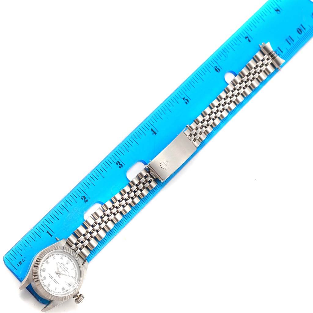 The image shows a top view of a Rolex Datejust 69174 Women's Stainless Steel White Dial 69174 Women's Stainless Steel White Dial watch with its band laid out alongside a blue ruler.