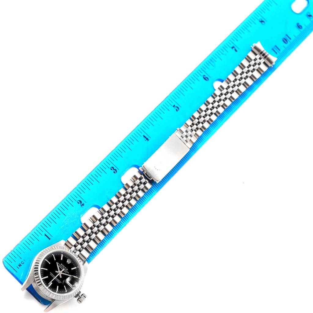 This image shows a Rolex Datejust 69174 Women's Stainless Steel Black Dial 69174 Women's Stainless Steel Black Dial watch, featuring its black dial and stainless steel bracelet, measured against a blue ruler.