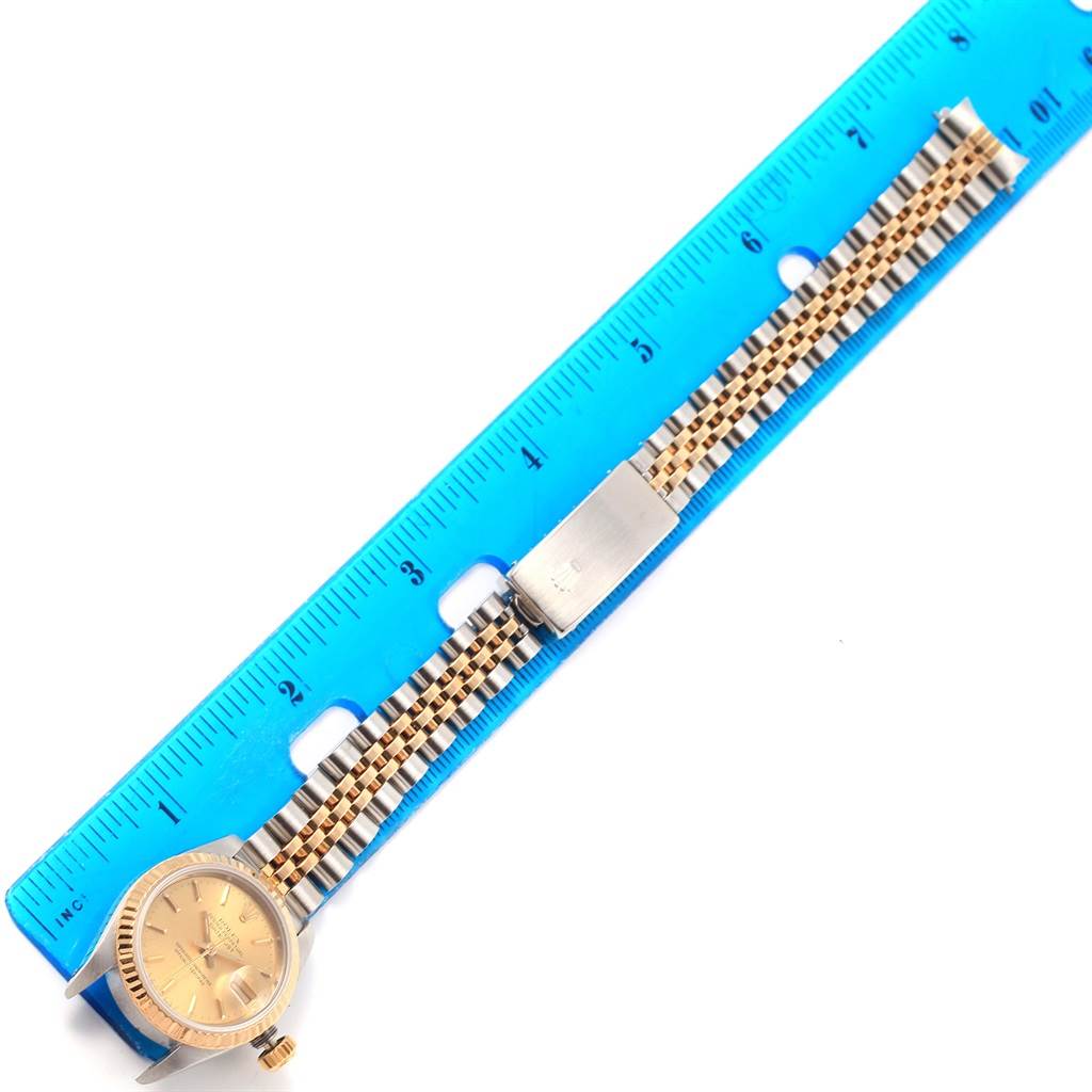 The image shows a Rolex Datejust 69173 Women's Stainless Steel Champagne Dial 69173 Women's Stainless Steel Champagne Dial watch with a gold face, alongside a two-tone bracelet, and it is placed next to a blue ruler.