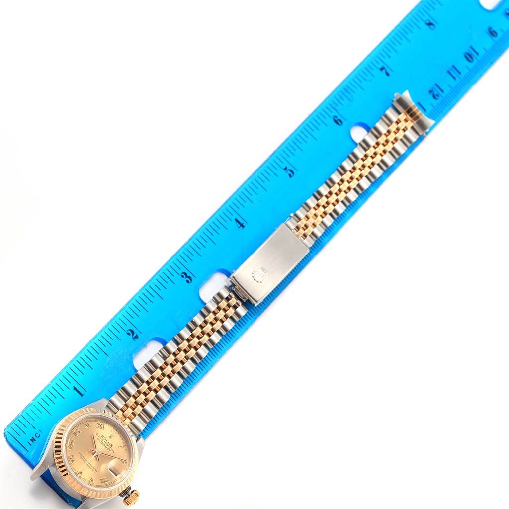 The image shows a Rolex Datejust 79173 Women's Steel and Gold (two tone) Champagne Dial 79173 Women's Steel and Gold (two tone) Champagne Dial watch displayed flat with a blue ruler, highlighting its band and clasp.