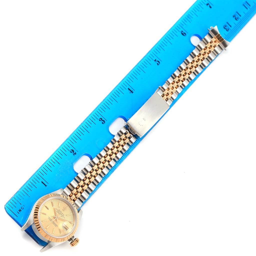 The Rolex Datejust 69173 Women's Stainless Steel Champagne Dial 69173 Women's Stainless Steel Champagne Dial model watch is shown from a top-down angle with a focus on its face and bracelet placed alongside a blue ruler.