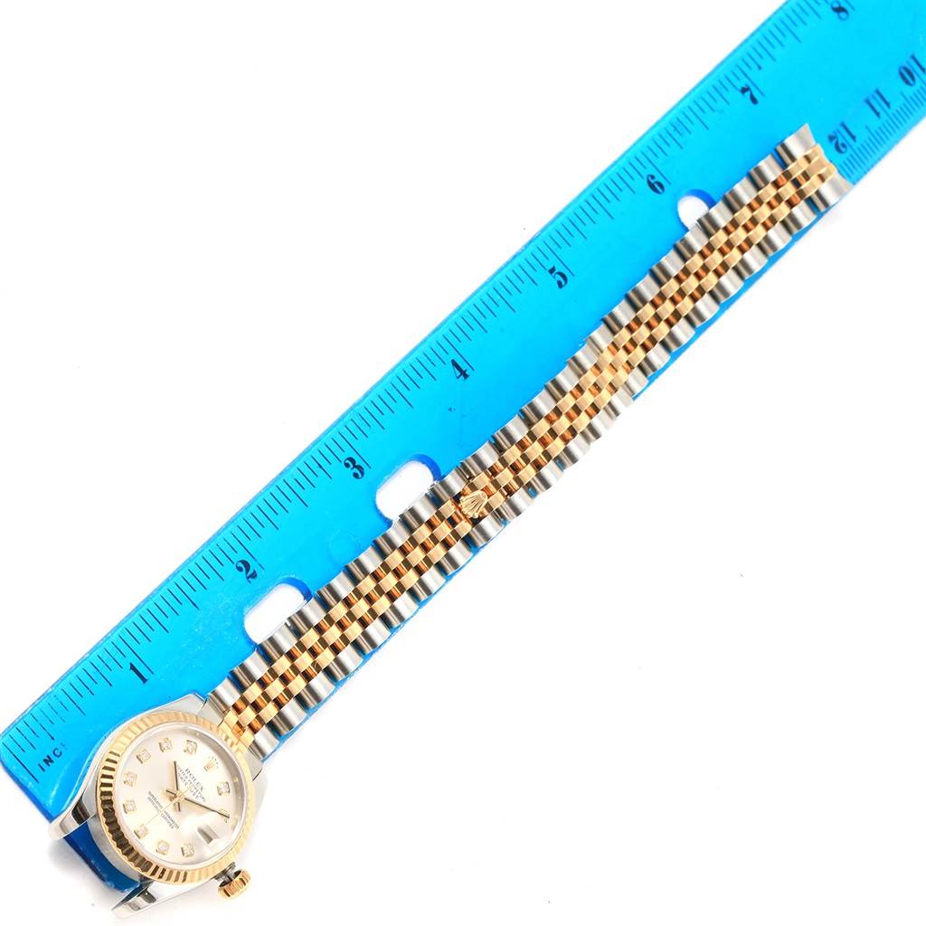 The image shows a Rolex Datejust 179173 Women's Steel and Gold (two tone) Silver Dial 179173 Women's Steel and Gold (two tone) Silver Dial watch with its face and two-tone bracelet measured against a blue ruler.