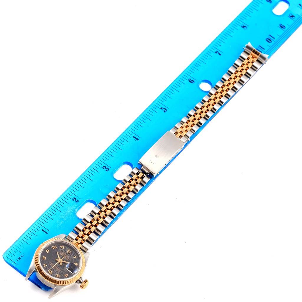 The Rolex Datejust 79173 Women's Stainless Steel Black Dial 79173 Women's Stainless Steel Black Dial watch is shown from a top-down angle, showcasing the face, bracelet, and clasp against a blue ruler.