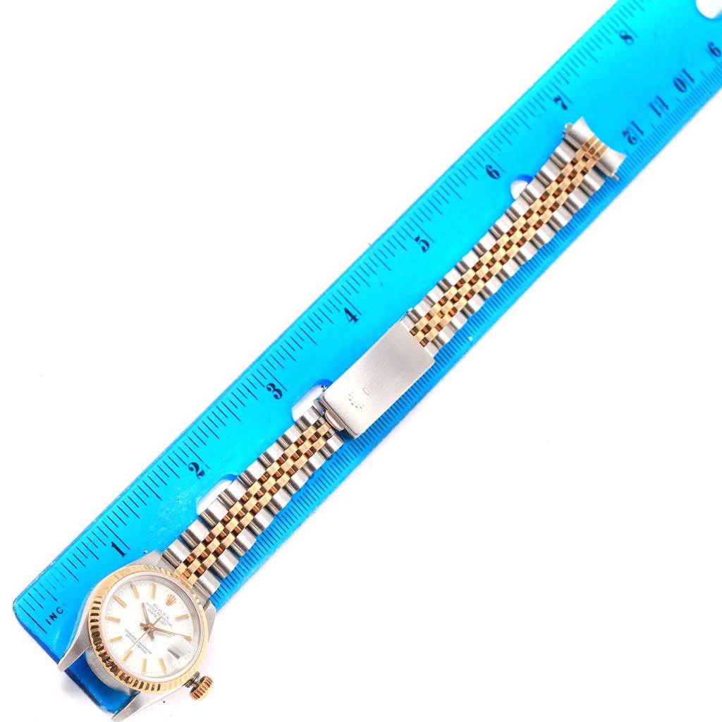 The Rolex Datejust 69173 Women's Stainless Steel White Dial 69173 Women's Stainless Steel White Dial watch is shown from a top-down angle, along with its two-tone bracelet and clasp, placed next to a blue ruler.