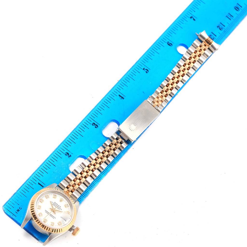 The image shows a Rolex Datejust 79173 Women's Stainless Steel White Dial 79173 Women's Stainless Steel White Dial watch with a view of the face and entire bracelet next to a blue ruler.