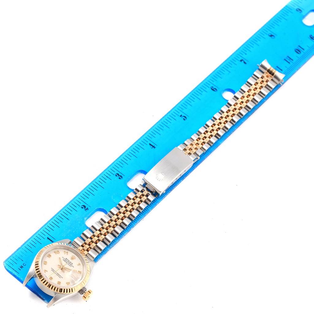 The Rolex Datejust 69173 Women's Stainless Steel Beige Dial 69173 Women's Stainless Steel Beige Dial watch is shown flat, displaying the face, bracelet, and clasp next to a blue ruler.