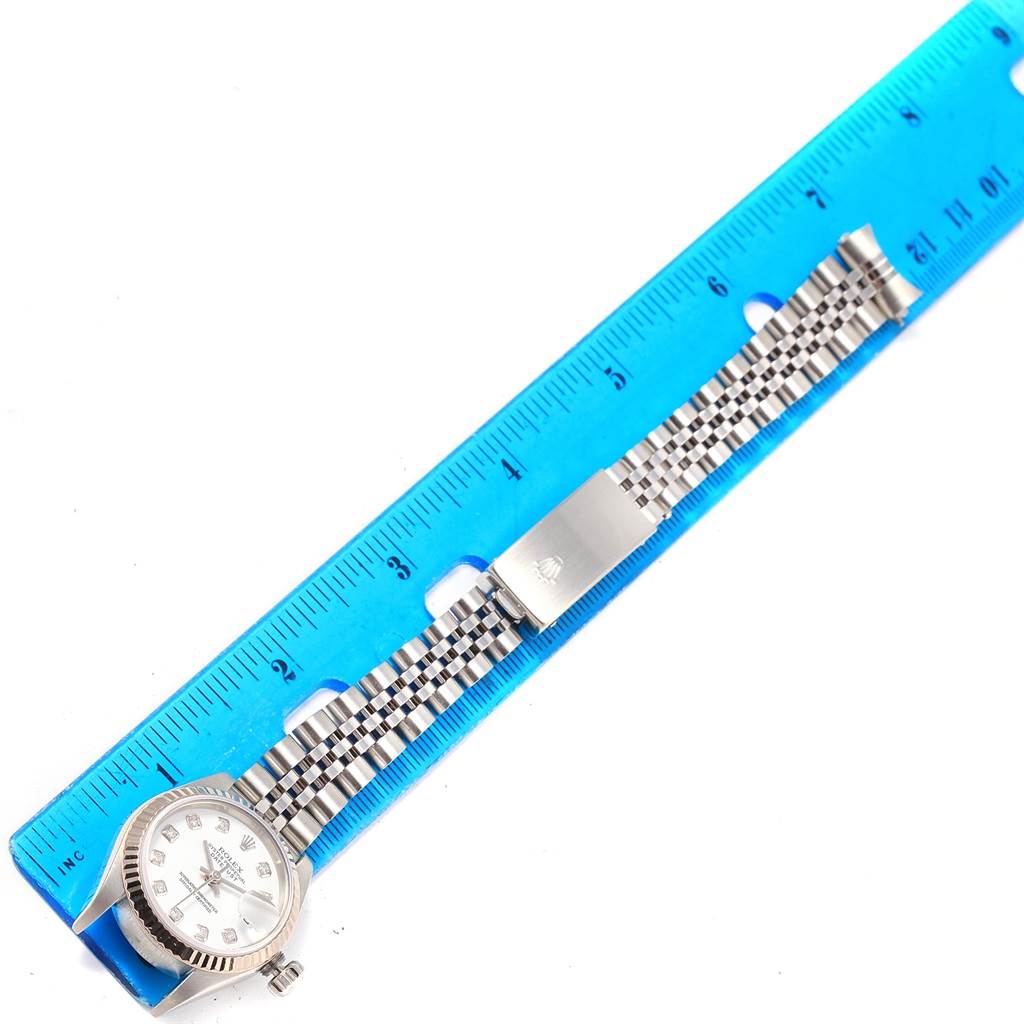 This image shows a Rolex Datejust 79174 Women's Stainless Steel White Dial 79174 Women's Stainless Steel White Dial watch and its jubilee bracelet laid next to a blue ruler for measurement.