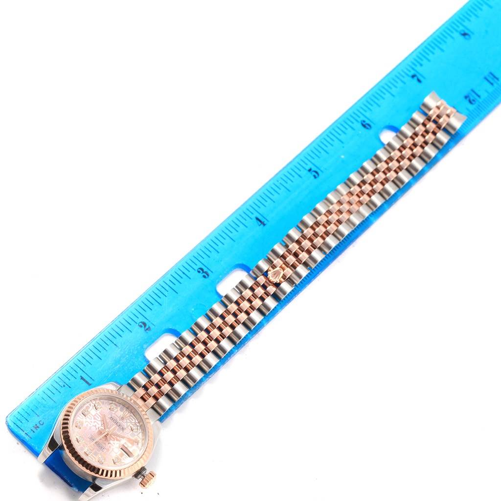 The Rolex Datejust 179171 Women
s Steel and Gold (two tone) Pink Dial 179171 Women
s Steel and Gold (two tone) Pink Dial watch is shown from the side, with its face and two-tone bracelet next to a blue ruler.