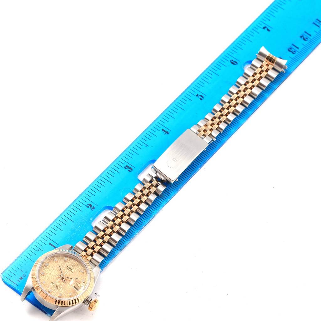 The Rolex Datejust 69173 Women's Stainless Steel Champagne Dial 69173 Women's Stainless Steel Champagne Dial watch is shown from a top-down view, displaying its face, bracelet, and clasp resting alongside a blue ruler.