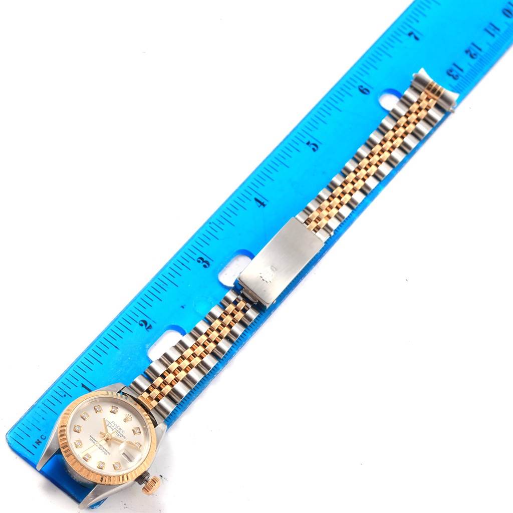 The Rolex Datejust 79173 Women's Stainless Steel Silver Dial 79173 Women's Stainless Steel Silver Dial watch is shown from a top-down angle, highlighting its face, bezel, and two-tone bracelet, alongside a blue ruler.