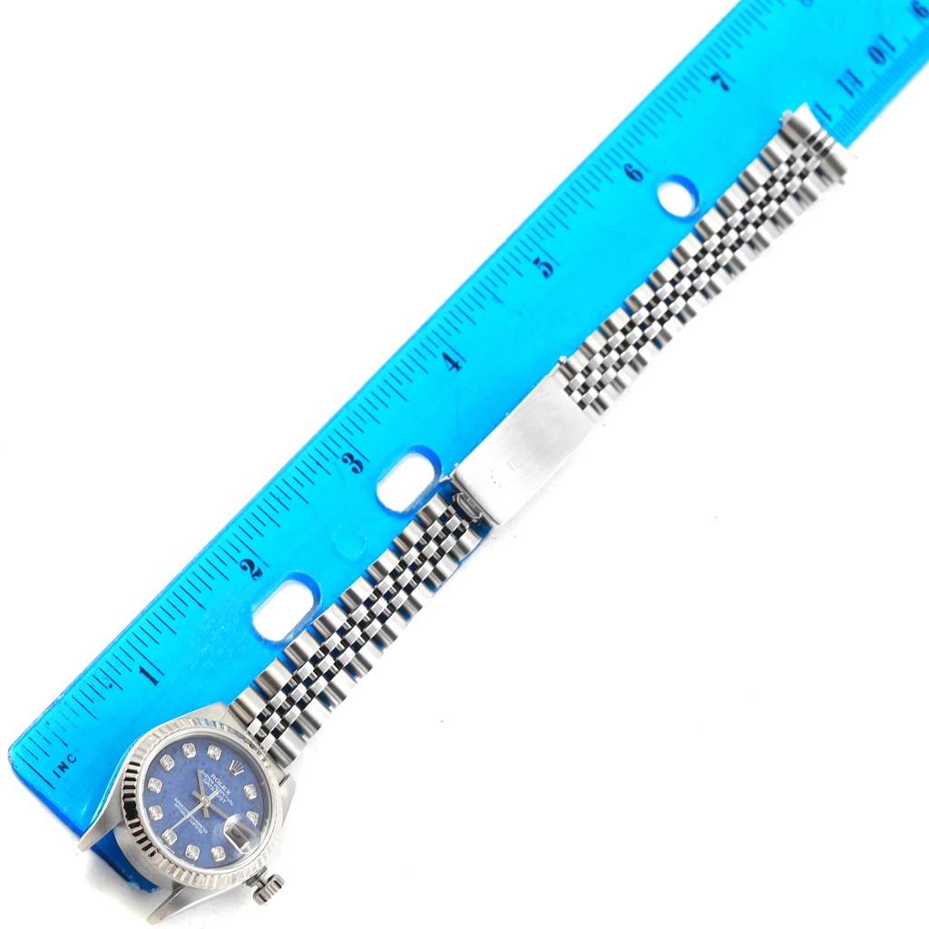 The image shows a Rolex Datejust 79174 Women's Stainless Steel Blue Dial 79174 Women's Stainless Steel Blue Dial watch with a blue dial and jubilee bracelet, laid flat next to a blue ruler.