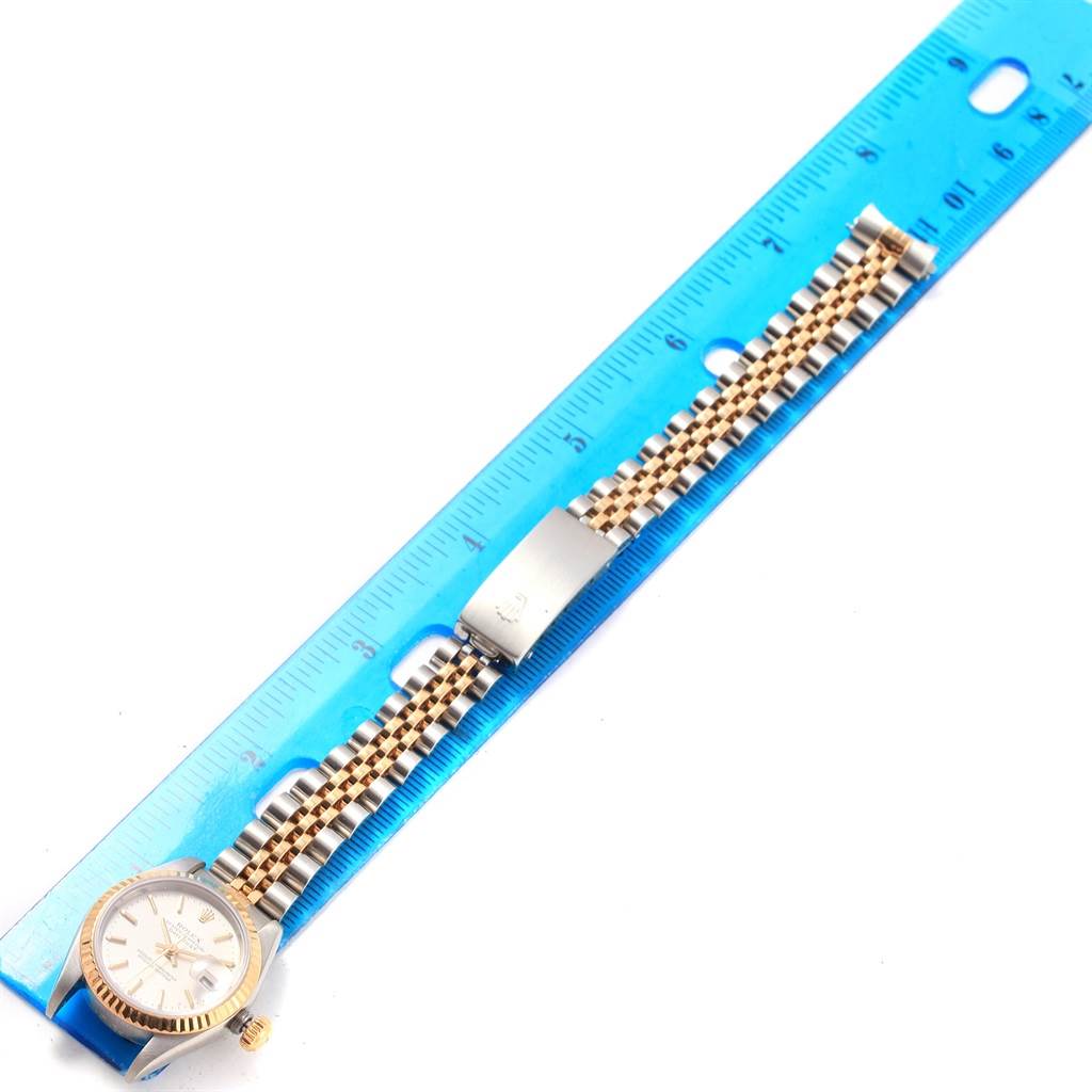 The image shows a top-down view of a Rolex Datejust 79173 Women's Steel and Gold (two tone) Silver Dial 79173 Women's Steel and Gold (two tone) Silver Dial watch with a two-tone bracelet and a blue ruler for measurement.