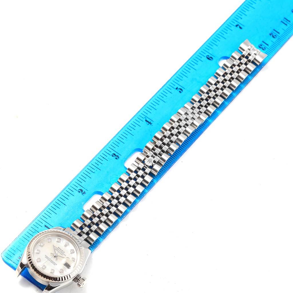 The image shows a Rolex Datejust 179174 Women
s Stainless Steel Mother of Pearl Dial 179174 Women
s Stainless Steel Mother of Pearl Dial watch laid flat with its bracelet alongside a ruler for measurement.