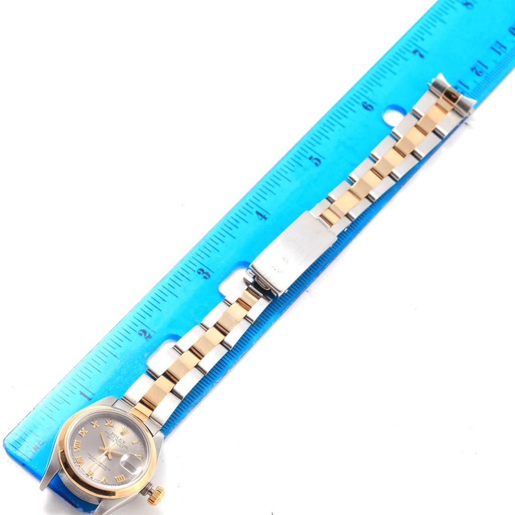 The Rolex Datejust 69163 Women's Stainless Steel Grey Dial 69163 Women's Stainless Steel Grey Dial watch is shown flat next to a blue ruler, displaying its face, bezel, and two-tone bracelet.