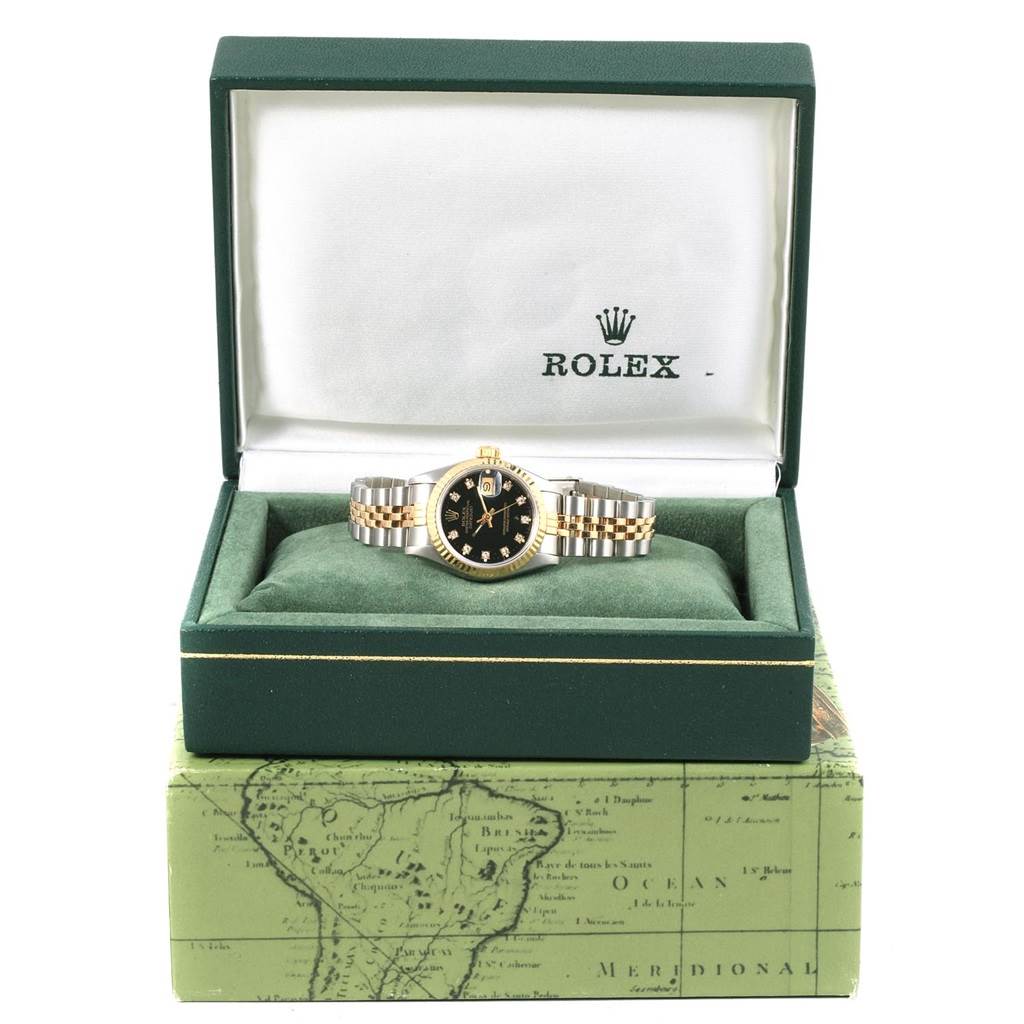 A Rolex Datejust 69173 Women's Stainless Steel Black Dial 69173 Women's Stainless Steel Black Dial watch is displayed face-up in its green and white box atop a green map-themed outer box.