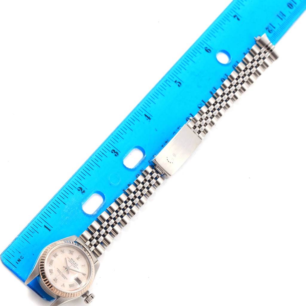 The Rolex Datejust 79174 Women's Stainless Steel Mother of Pearl Dial 79174 Women's Stainless Steel Mother of Pearl Dial watch is displayed flat with the face, bezel, bracelet, and clasp visible next to a blue ruler for scale.