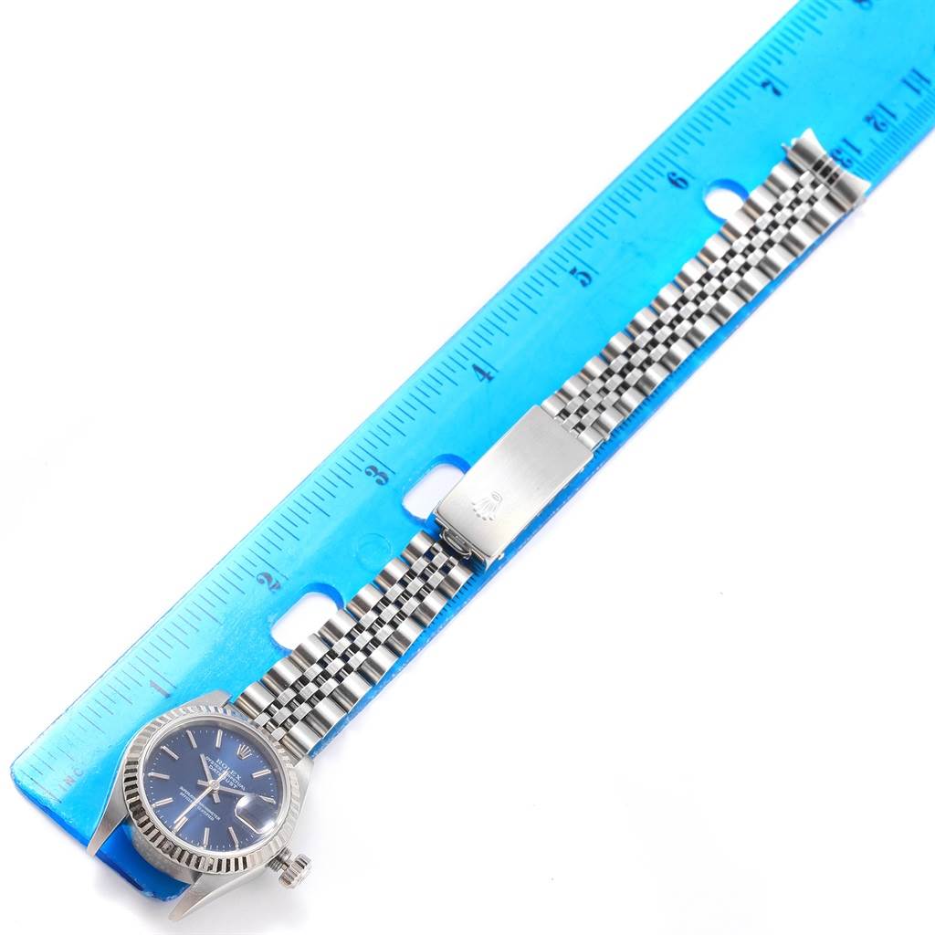 The Rolex Datejust 79174 Women
s Stainless Steel Blue Dial 79174 Women
s Stainless Steel Blue Dial watch is shown from a top-down angle, highlighting the face, bezel, and metal bracelet placed beside a ruler.