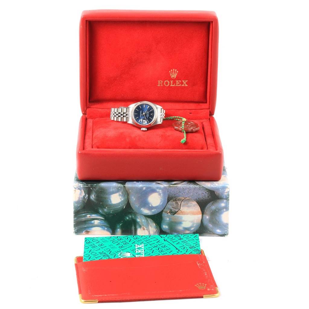 The image shows a Rolex Datejust 79174 Women
s Stainless Steel Blue Dial 79174 Women
s Stainless Steel Blue Dial watch in a red display box, with additional accessories including a booklet and packaging.