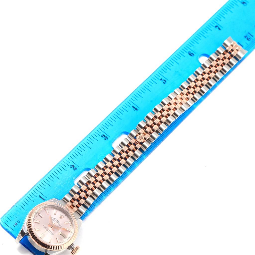 The Rolex Datejust 179171 Women's Steel and Gold (two tone) Pink Dial 179171 Women's Steel and Gold (two tone) Pink Dial watch is shown from a top-down angle, displaying the face and entire bracelet against a blue ruler.