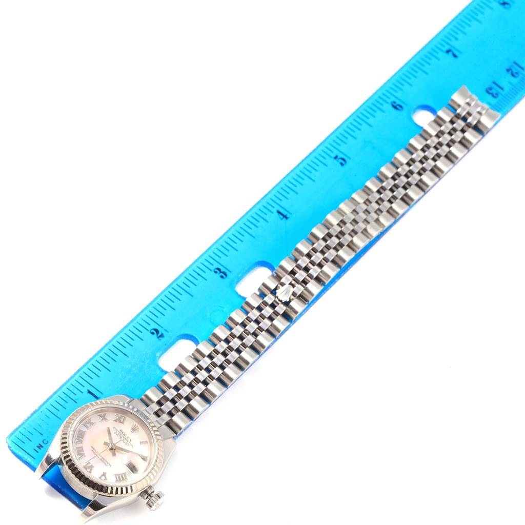 The Rolex Datejust 179174 Women
s Stainless Steel Mother of Pearl Dial 179174 Women
s Stainless Steel Mother of Pearl Dial watch is shown flat with its face and entire band against a blue ruler for measurement.