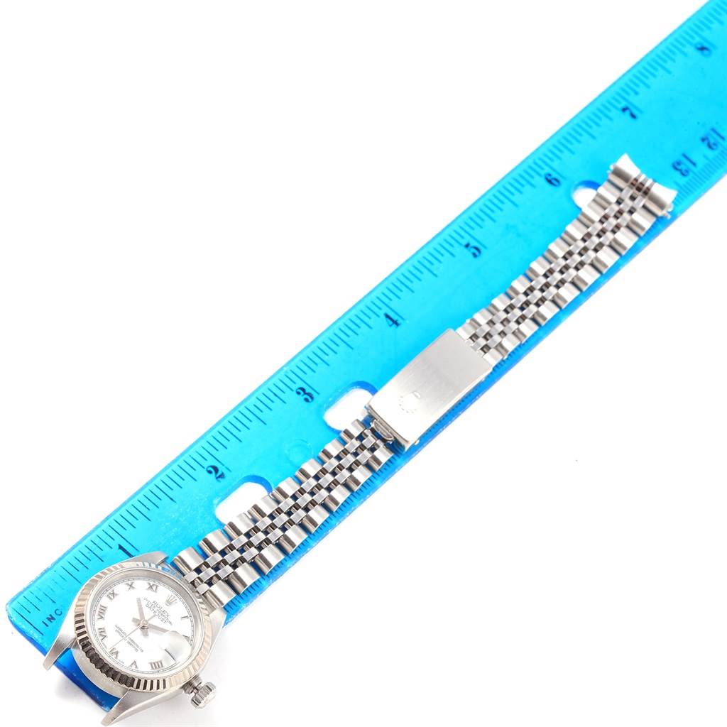 This image shows the Rolex Datejust 79174 Women
s Stainless Steel White Dial 79174 Women
s Stainless Steel White Dial watch laid flat with its face, bezel, and bracelet, beside a blue ruler for scale.